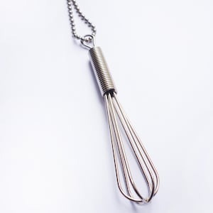 Può includere: Una collana con un ciondolo a forma di frusta in argento e una catena in argento.