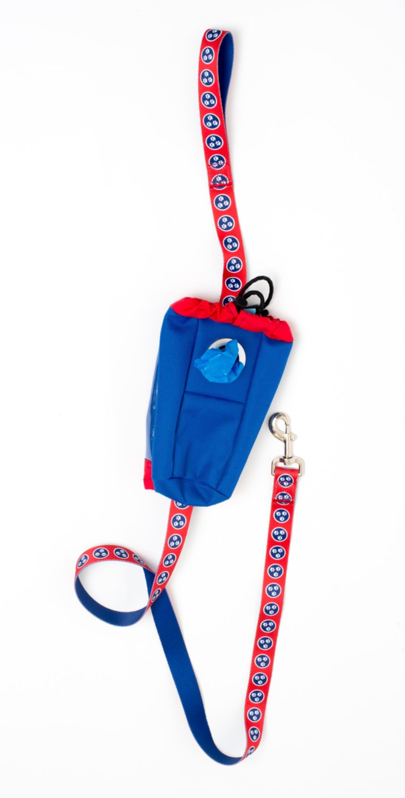 May include: A red and blue dog leash with a matching blue and red poop bag dispenser. The leash has a repeating pattern of paw prints.