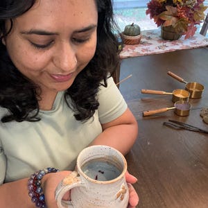 Puede incluir: Una taza de cer&aacute;mica blanca con esmalte marr&oacute;n moteado y un l&iacute;quido azul en su interior. La taza tiene un asa y est&aacute; decorada con un peque&ntilde;o dise&ntilde;o marr&oacute;n.