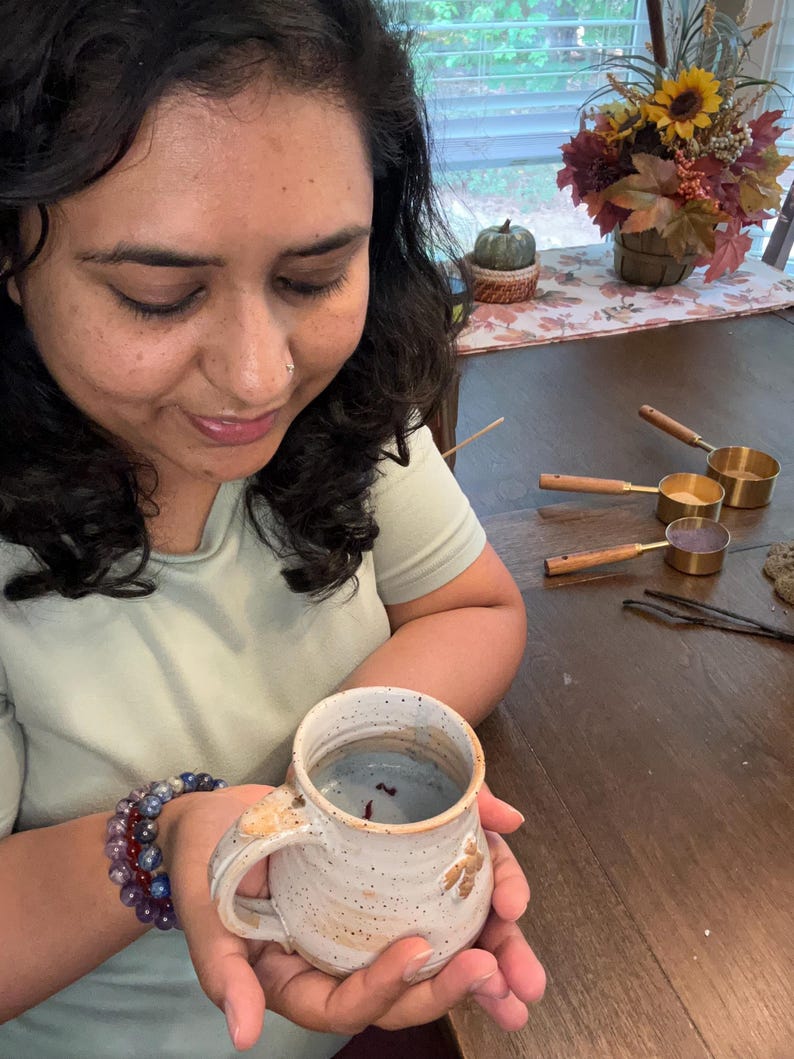 Puede incluir: Una taza de cer&aacute;mica blanca con esmalte marr&oacute;n moteado y un l&iacute;quido azul en su interior. La taza tiene un asa y est&aacute; decorada con un peque&ntilde;o dise&ntilde;o marr&oacute;n.