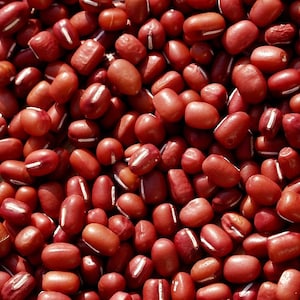Può includere: Un'immagine ravvicinata di un mucchio di fagioli rossi. I fagioli sono piccoli e di forma ovale, con una striscia bianca che corre lungo il centro di ogni fagiolo.