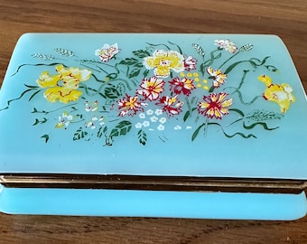 May include: A light blue trinket box with a floral design. The box has a gold trim and a hinged lid.