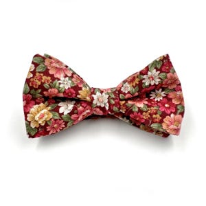 May include: A burgundy bow tie with a floral pattern featuring pink, white, and yellow flowers.