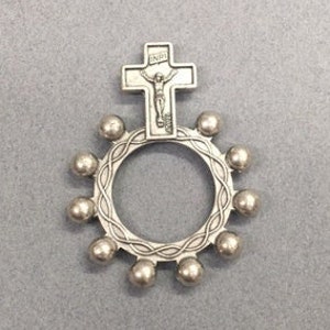 May include: A silver rosary ring with a crucifix featuring a figure of Jesus Christ. The ring has a circle of beads around the crucifix.