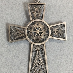 May include: A silver filigree cross pendant with a detailed design. The cross is made of thin, intertwined wires that create a delicate and intricate pattern.