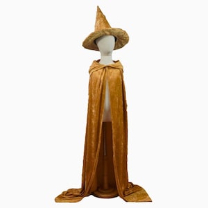 May include: A golden-colored witch costume set, including a pointed hat and a long cape with a hood. The costume is displayed on a mannequin, showcasing the flowing fabric and design. Perfect for Halloween or costume parties.