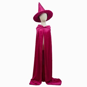 May include: A magenta witch costume set, including a pointed hat with a wide brim and a long cape with a hood. The costume is displayed on a mannequin against a white background. The fabric appears to be a soft velvet.