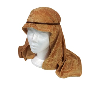 May include: A golden-brown crushed velvet head covering featuring a draped, hood-like design that extends down to the shoulders. A thin, dark brown cord encircles the crown of the head, securing the fabric in place around the forehead.