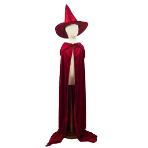 May include: A red velvet witch costume set, including a pointed hat and a long cape. The costume is displayed on a mannequin against a white background. The hat has a wide brim and a tall, conical crown.
