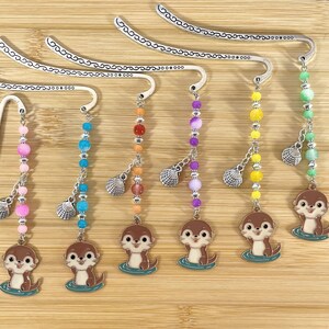 May include: Six decorative metal bookmarks with colorful beaded strands and otter charms. Each bookmark features a different color scheme, including pink, blue, orange, purple, yellow, and green beads, and a small seashell charm.