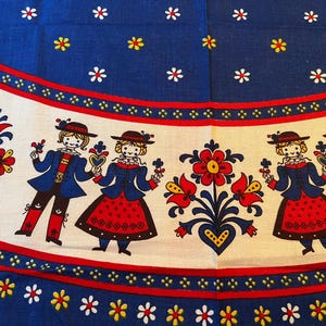 Può includere: Una tovaglia bianca con un bordo blu e rosso. Il bordo presenta un motivo ripetitivo di piccoli fiori bianchi e cuori rossi. Il centro della tovaglia presenta un motivo ripetitivo di fiori stilizzati e figure in costumi tradizionali popolari.