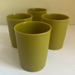 以下が含まれることがあります： 4つのオリーブグリーンのプラスチックカップ。カップは円筒形で、上部がわずかに広がっています。カップは空で、白い表面に配置されています。カップは無地の不透明な素材で作られています。
