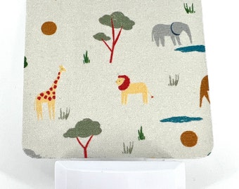 May include: A white night light with a removable fabric cover featuring a safari animal print. The cover has giraffes, lions, elephants, trees, and a sun. The night light has a small button on the front.