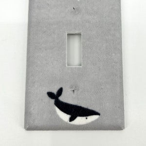 Puede incluir: Una tapa de interruptor de luz gris con una estrella blanca y un diseño de ballena blanco y negro.
