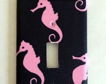 May include: A black light switch cover with a pink seahorse pattern. The cover has a single light switch opening.
