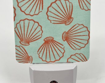 May include: A white nightlight with a light blue fabric cover featuring a repeating pattern of orange seashells.