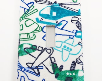 May include: White light switch cover with a blue, green, and black pattern of airplanes and helicopters.