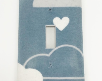 May include: A light blue light switch cover with a white heart and white clouds on a blue background.