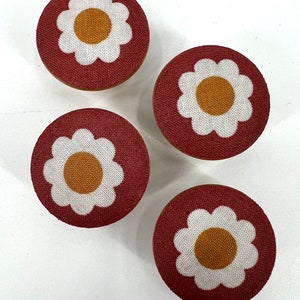 Peut inclure: Quatre boutons de tiroir ronds en tissu rouge avec des motifs de marguerites blanches et des centres jaunes.