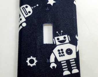 May include: A black light switch cover with a white robot design. The robots are in different poses and have a star and gear design in the background.