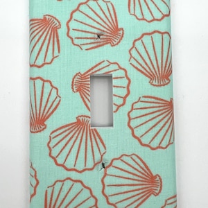 Puede incluir: Una tapa de interruptor de luz azul claro con un patrón de conchas de mar naranjas.