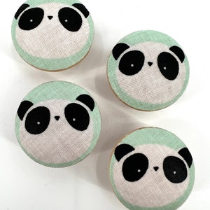 May include: Four round fabric buttons with a panda bear face design. The buttons are white with black panda features and a light green border.
