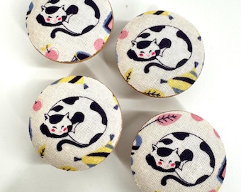 May include: Four round wooden knobs with a white fabric covering featuring a black and white cat design. The fabric has a colorful geometric pattern with pink, yellow, and blue accents.