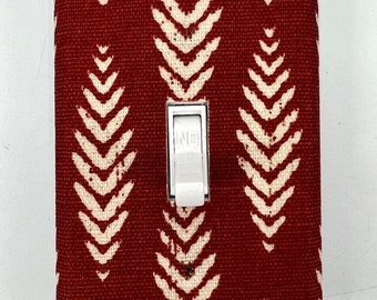 May include: A white light switch with a red fabric cover. The fabric has a white chevron pattern.