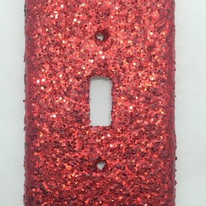 May include: Red glitter light switch cover plate. The plate has a single switch opening and two screw holes.
