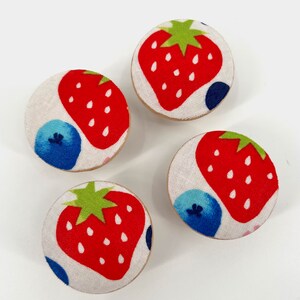 May include: Four round fabric covered knobs with a white background and a red strawberry, green leaves, and blue and white blueberries pattern.