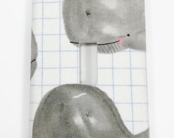 May include: A white light switch cover with a blue grid pattern and two gray whale illustrations. The whales have pink cheeks and black eyes.