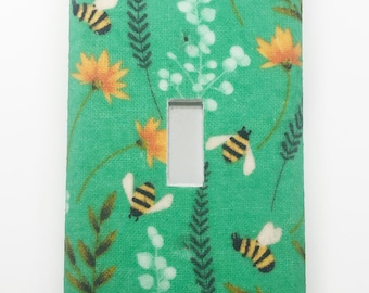 May include: A green light switch cover with a floral pattern featuring bees and flowers.