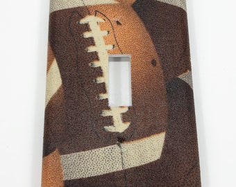 May include: A light switch cover with a brown and white football pattern.