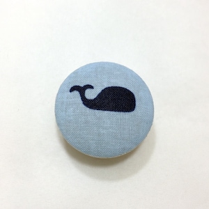 May include: A light blue fabric button with a black whale silhouette.