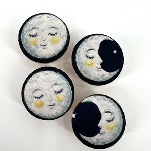 May include: Four fabric-covered moon-shaped knobs with a sleeping face and a star. The knobs are in shades of white, gray, black, and yellow.