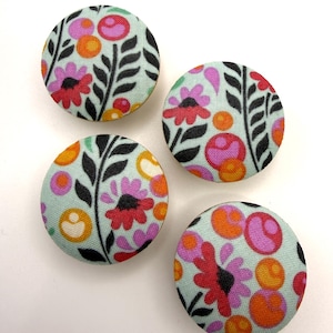 May include: Four round fabric buttons with a floral pattern. The buttons have a light blue background with a repeating pattern of red, pink, orange, and white flowers, and black leaf stems.