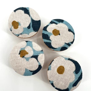 May include: Four round fabric buttons with a white background and a blue and white floral pattern. The center of each flower has a small yellow circle.