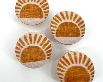 May include: Four round fabric coasters with a sun design. The coasters are white with a brown sun design.