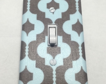 May include: A light blue and gray patterned light switch cover. The cover has a geometric design with a white light switch in the center.