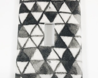 May include: A white light switch cover with a black and white geometric pattern of triangles.