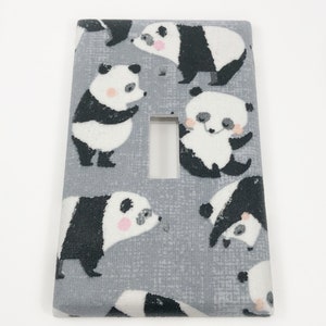 Op de afbeelding: Een lichtgrijze lichtschakelaar-afdekplaat met een herhalend patroon van zwart-witte pandaberen. De panda's staan in verschillende poses, sommige staan, sommige zitten en sommige kijken naar de kijker.