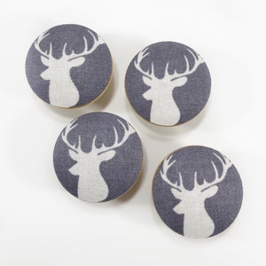 May include: Four gray fabric covered knobs with white deer silhouettes. The deer are facing left and have antlers.