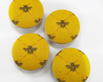 May include: Four yellow fabric covered buttons with a black bee design. The bees are in a repeating pattern on the buttons.