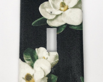 May include: A black light switch cover with a white magnolia flower design.