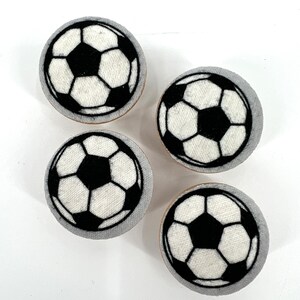 May include: Four white fabric covered buttons with black soccer ball designs.