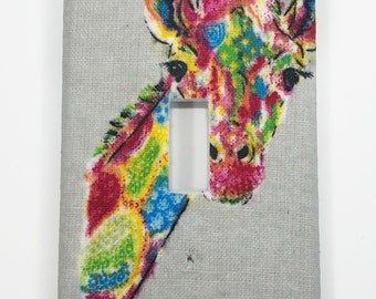 May include: A light gray light switch cover with a colorful giraffe illustration. The giraffe's head and neck are visible, with a colorful pattern of pink, blue, yellow, and green.
