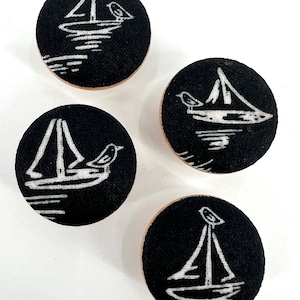 Könnte beinhalten: Vier schwarze runde Stoffknöpfe mit weißen Segelboot- und Vogelmotiven.