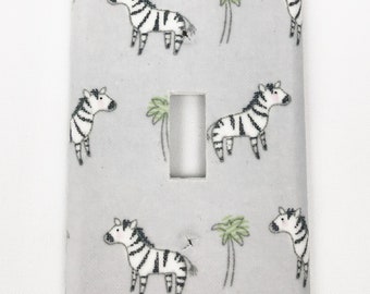 May include: A light gray light switch cover with a pattern of black and white zebras and green palm trees.
