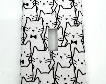 May include: White light switch cover with a black and white pattern of cats wearing bow ties.