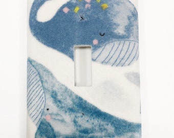 May include: A white light switch cover with a blue whale pattern. The whales are illustrated in a watercolor style with yellow and pink accents.